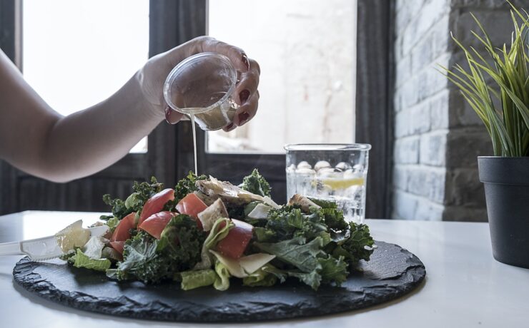 Persona che versa la salsa di vinaigrette per insalata di verdure, olio per insalata