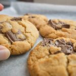 persona che tiene biscotti marroni su tessuto bianco