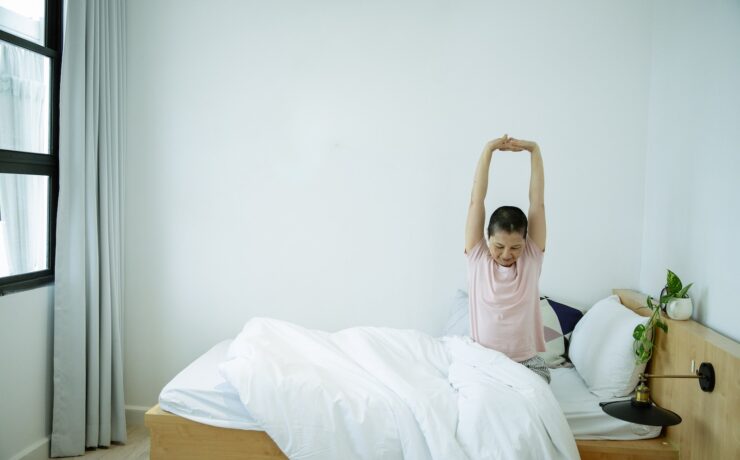 Ethnic female stretching body on bed in morning plant bedroom recovery healthy body