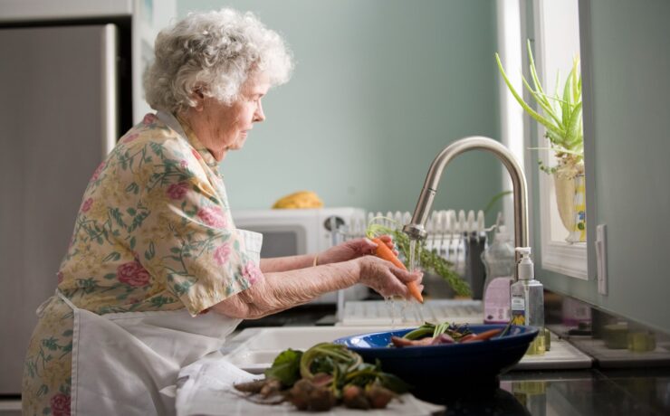 donna che indossa un abito floreale giallo e rosa che lava la cucina delle carote