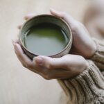 Alto angolo di raccolto donna anonima in maglieria con tazza in ceramica di tè verde tè matcha caldo