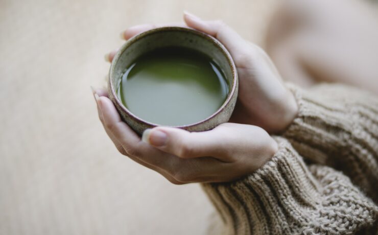 Alto angolo di raccolto donna anonima in maglieria con tazza in ceramica di tè verde tè matcha caldo