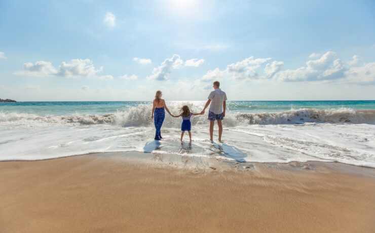 uomo, donna e bambino che si tengono per mano sull'oceano in riva al mare