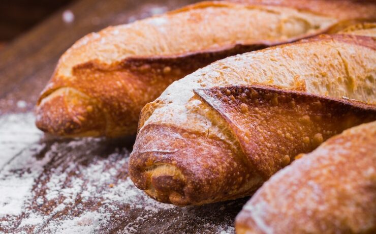 Foto ravvicinata di tre baguette su superficie di legno marrone con pane bianco in polvere Francia