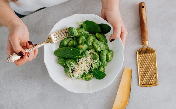 Una persona che tiene un piatto e una forchetta con gnocchi al basilico Green Food