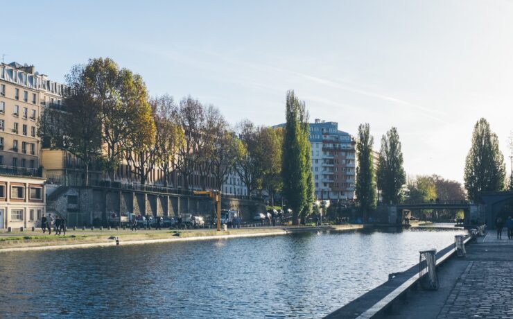 persone che camminano vicino alla strada circondata da edifici e alberi che osservano il lago calmo