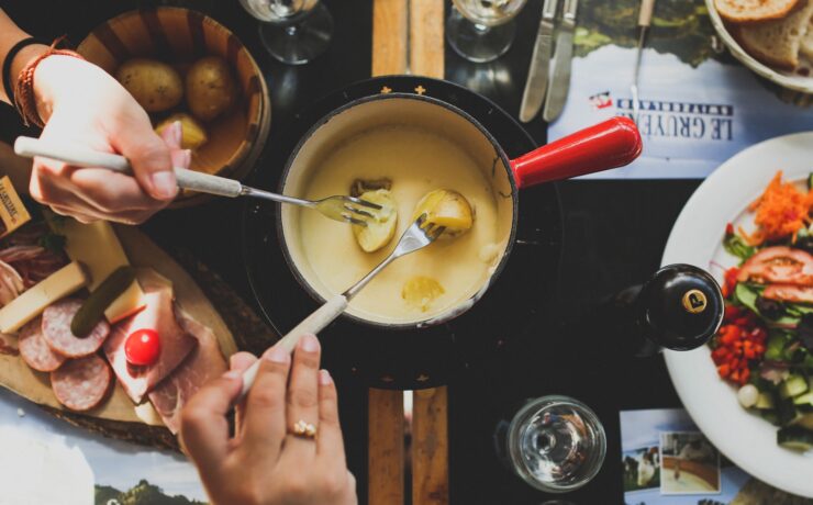 due persone che tengono la forchetta immergendo il cibo in salsa fonduta di formaggio cena pranzo