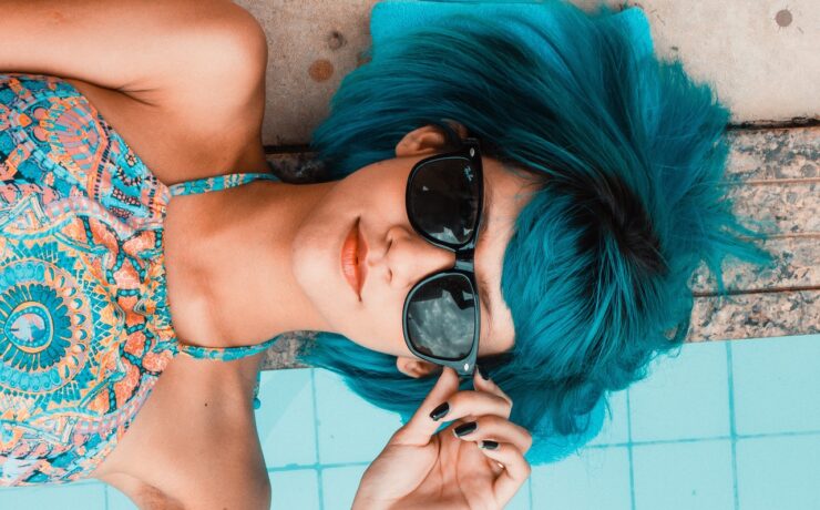 garota de cabelo azul e óculos Rayban deitada na beira de uma piscina