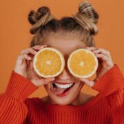 Mulher com suéter de tricô vermelho segurando duas fatias de laranja sobre os olhos