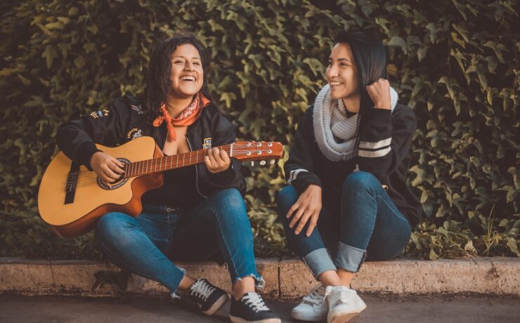 mulher tocando violão sentada ao lado de uma mulher sorrindo