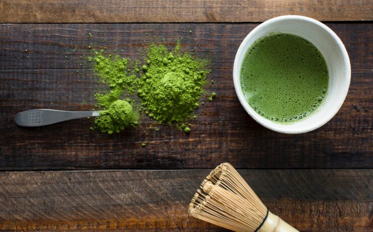 chá verde em caneca de cerâmica branca ao lado de pincel de madeira marrom e pó de matcha