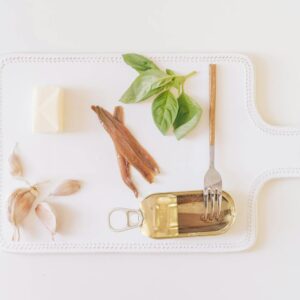 Flat lay of fresh ingredients including anchovies, garlic, butter, and basil on a white cutting board.