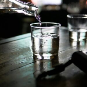 A clear glass of water being poured from a bottle, set on a rustic wooden table in a dimly lit indoor setting.