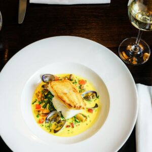 Exquisite seafood dish with clams and fish served at an elegant London restaurant, paired with white wine.