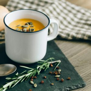 Warm pumpkin soup garnished with seeds and herbs in an enamel mug, perfect for fall comfort food.