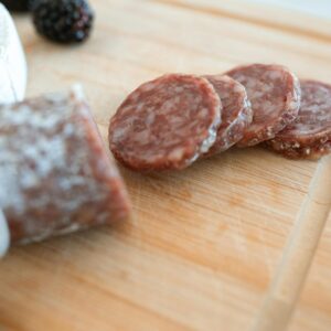 Close-up of an artisanal charcuterie board featuring sliced salami, cheese, and fresh blackberries on a wooden cutting board.