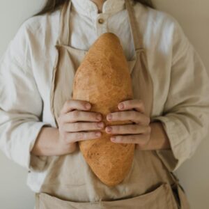 Close-up of a person in an apron holding a freshly baked loaf of bread.