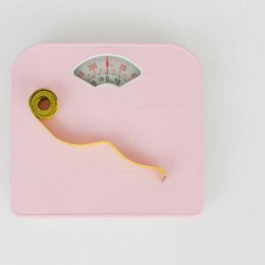 A pink weighing scale paired with a yellow measuring tape on a white backdrop.