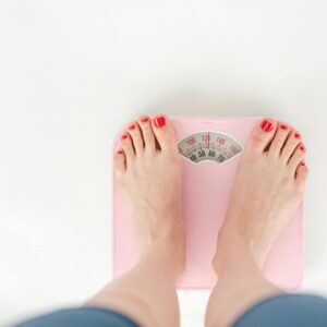 Top view of crop anonymous barefoot female measuring weight on scales on white background