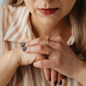 Close-up of a woman with clasped hands wearing rings, showing thoughtful expression.