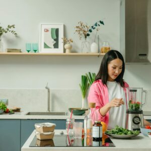 Asian woman blending fresh fruits and vegetables in a stylish kitchen setting.