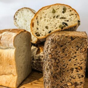 Close-up of various artisan bread loaves and slices on a wooden board, featuring fresh and baked textures.